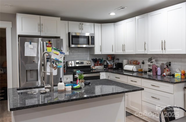 kitchen featuring visible vents, dark stone countertops, stainless steel appliances, white cabinetry, and backsplash