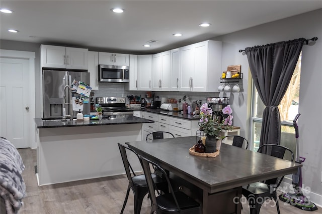 kitchen with tasteful backsplash, light wood-style flooring, appliances with stainless steel finishes, white cabinetry, and a kitchen island