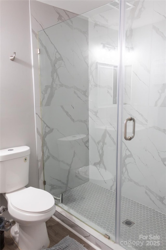 bathroom featuring toilet, a marble finish shower, and wood finished floors