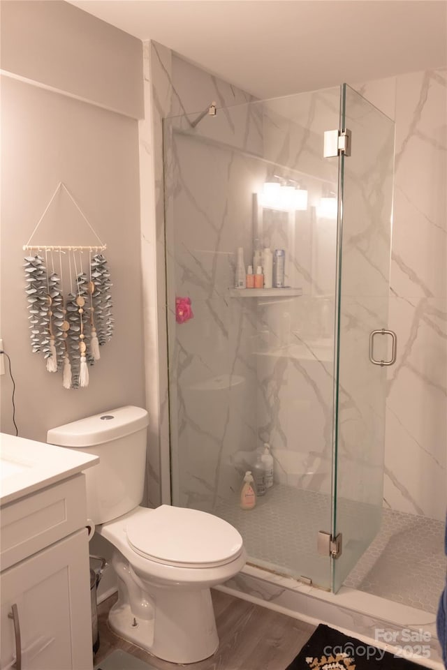 full bath featuring toilet, a marble finish shower, and vanity