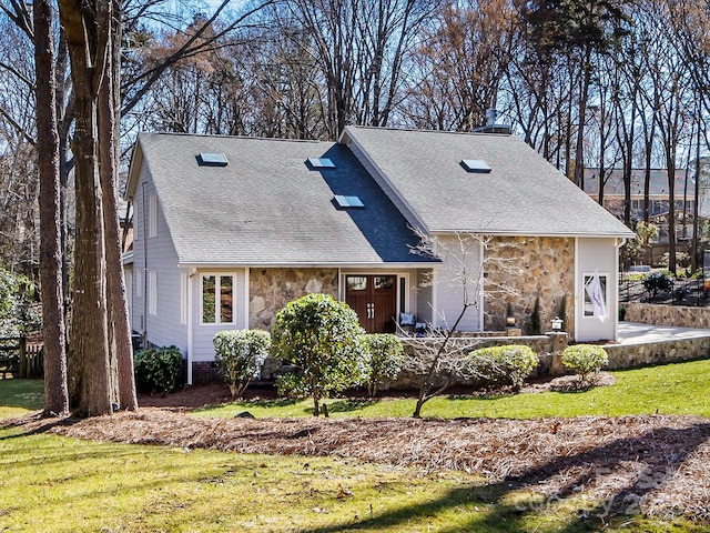 view of front of house with stone siding, a shingled roof, and a front yard