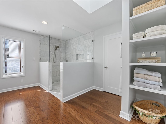 bathroom with a skylight, wood finished floors, visible vents, baseboards, and walk in shower