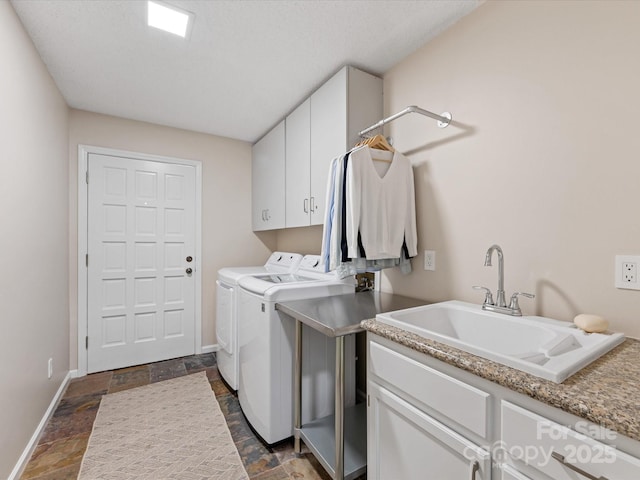 laundry room with cabinet space, baseboards, stone finish flooring, washing machine and dryer, and a sink