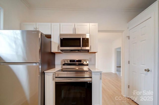 kitchen with white cabinets, light wood-style flooring, appliances with stainless steel finishes, light countertops, and crown molding