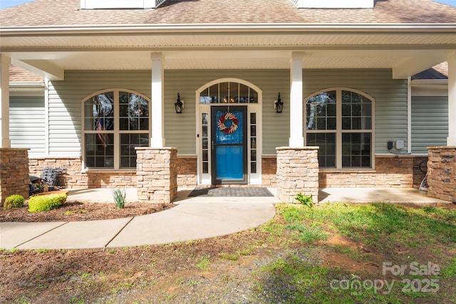 entrance to property with a shingled roof and a porch