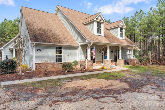 cape cod-style house featuring covered porch, stone siding, and roof with shingles