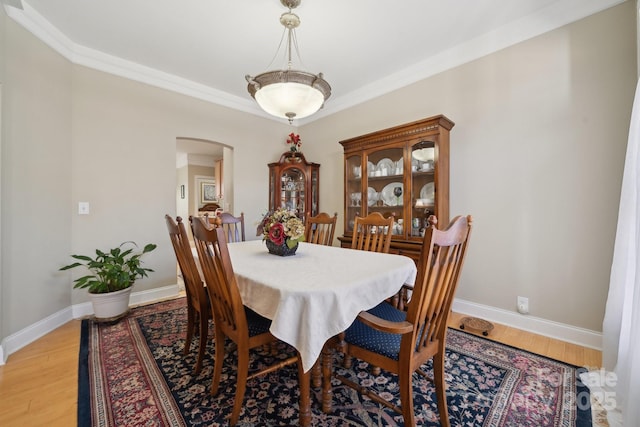 dining space with arched walkways, light wood-type flooring, and baseboards