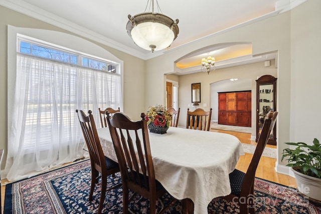 dining space featuring arched walkways, ornamental molding, wood finished floors, and baseboards