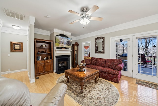 living area with light wood finished floors, visible vents, a fireplace with flush hearth, ornamental molding, and a ceiling fan
