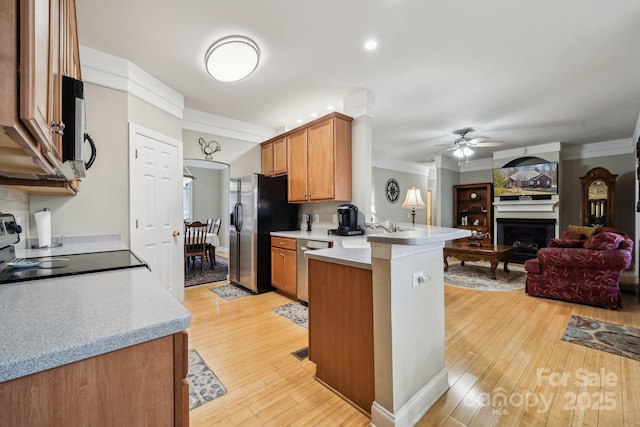 kitchen featuring a peninsula, stainless steel appliances, a sink, open floor plan, and light countertops