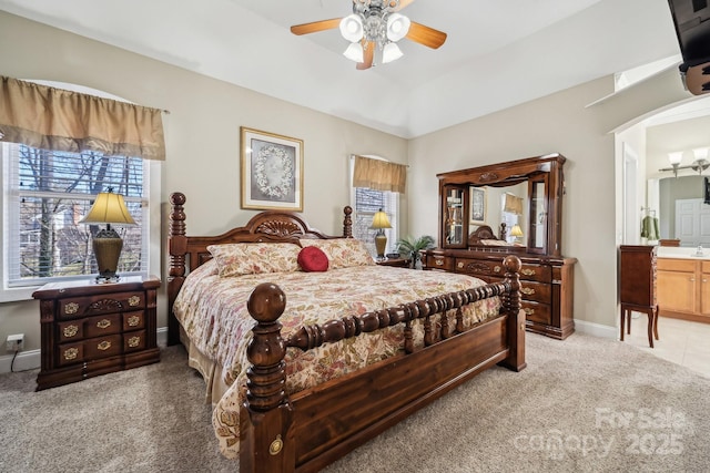 carpeted bedroom with baseboards, arched walkways, lofted ceiling, ceiling fan, and ensuite bath