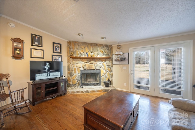 living area with crown molding, a stone fireplace, a textured ceiling, and wood finished floors