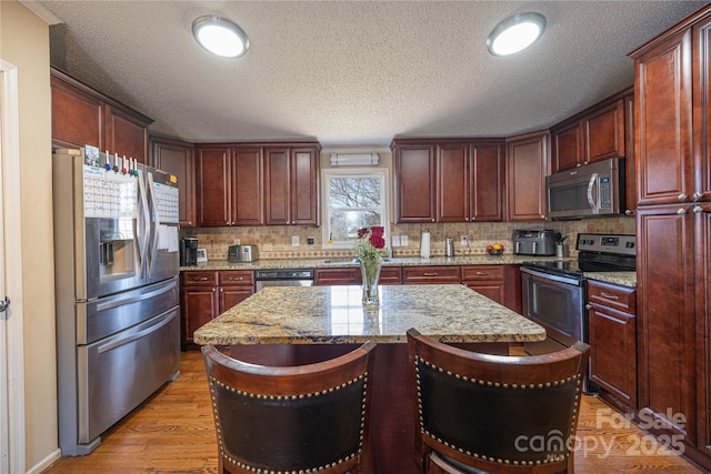 kitchen featuring decorative backsplash, light wood-style flooring, a kitchen island, a breakfast bar, and stainless steel appliances