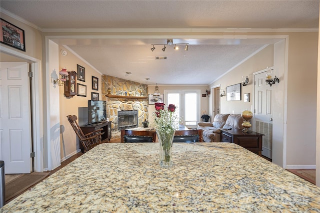 dining area featuring a textured ceiling, a stone fireplace, visible vents, baseboards, and crown molding