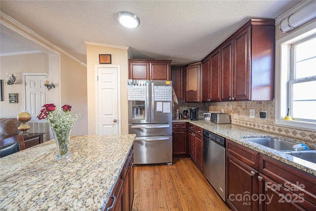 kitchen featuring tasteful backsplash, light wood-style flooring, appliances with stainless steel finishes, ornamental molding, and light stone countertops