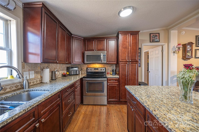 kitchen with stainless steel appliances, light wood-style floors, a sink, and backsplash