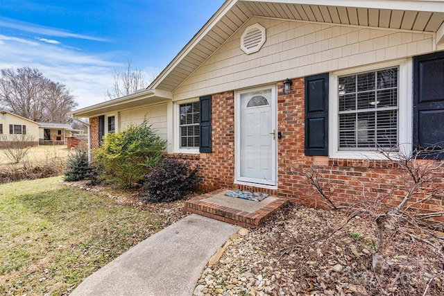 view of exterior entry with brick siding and a yard