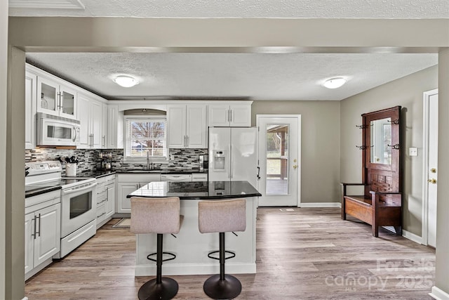 kitchen with white appliances, white cabinetry, a kitchen island, and glass insert cabinets