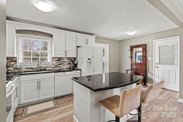 kitchen featuring white appliances, a kitchen island, light wood-style floors, white cabinetry, and a sink