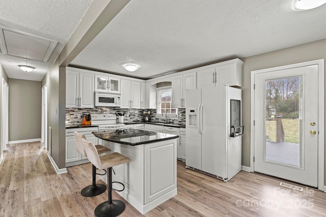 kitchen with white appliances, a kitchen island, a breakfast bar area, and white cabinets