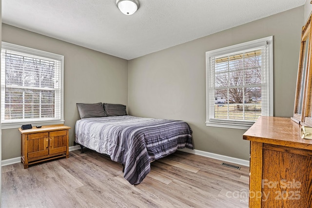 bedroom with baseboards, multiple windows, visible vents, and light wood-style floors