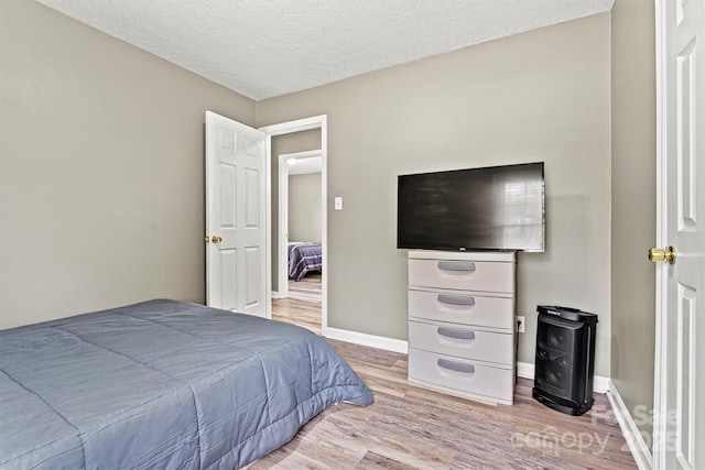 bedroom featuring baseboards, a textured ceiling, and light wood-style floors