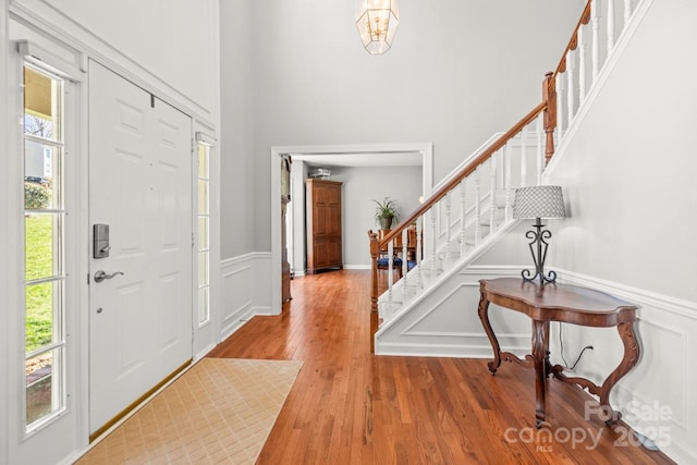 entryway featuring stairs, wainscoting, a decorative wall, and wood finished floors