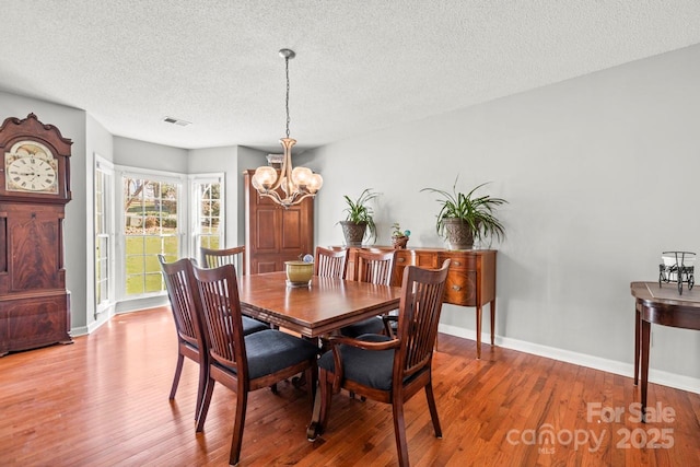 dining room with baseboards, visible vents, a textured ceiling, light wood-style floors, and a notable chandelier