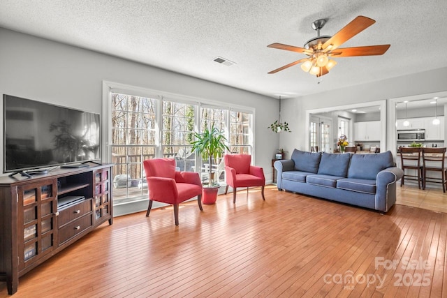 living area featuring light wood finished floors, ceiling fan, visible vents, and a textured ceiling