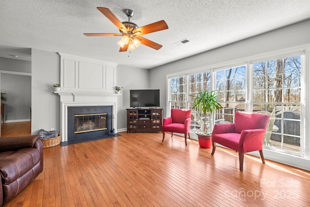 living area featuring a textured ceiling, a fireplace, visible vents, a ceiling fan, and light wood-type flooring