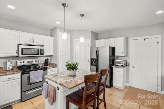 kitchen with a breakfast bar area, stainless steel appliances, white cabinetry, a kitchen island, and light stone countertops