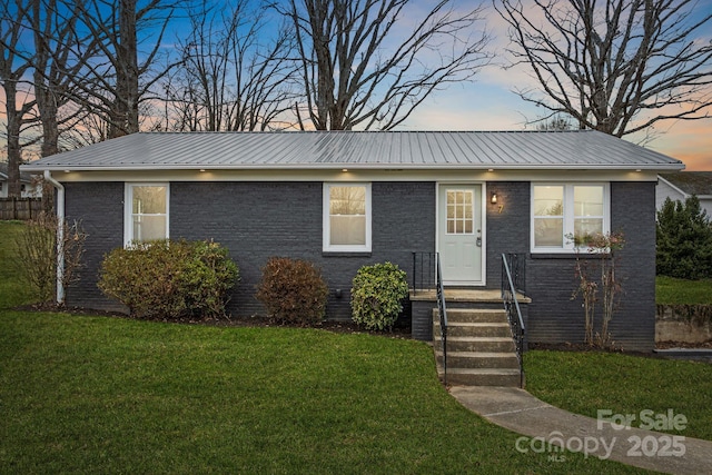 view of front of house with a lawn, brick siding, and metal roof