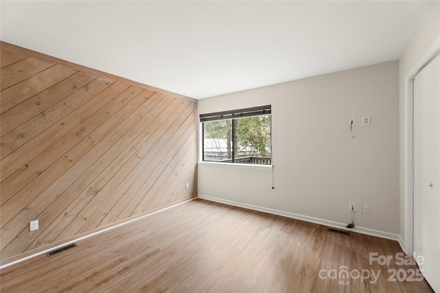 unfurnished room featuring wood walls, wood finished floors, visible vents, and baseboards