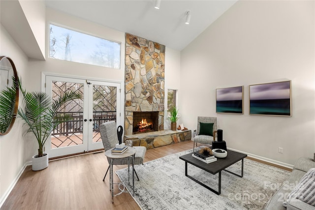 living room with high vaulted ceiling, a fireplace, wood finished floors, baseboards, and french doors