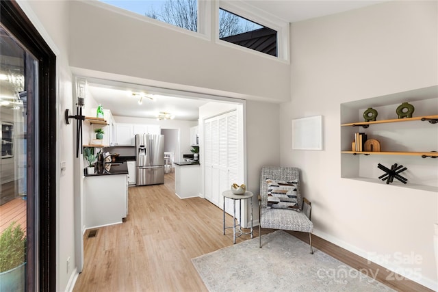 living area featuring a towering ceiling, light wood-style floors, visible vents, and baseboards