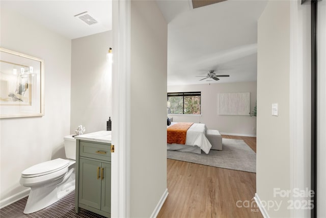 ensuite bathroom featuring visible vents, toilet, ceiling fan, vanity, and ensuite bath