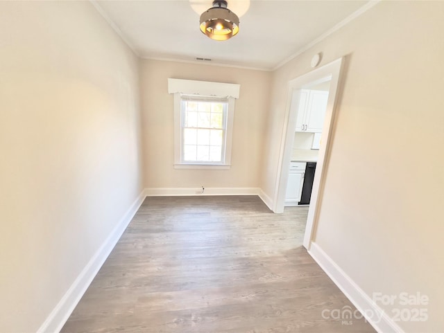 empty room featuring baseboards, light wood-style floors, visible vents, and crown molding