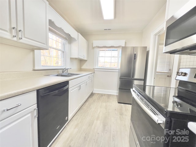 kitchen with stainless steel appliances, light countertops, light wood-style floors, white cabinets, and a sink