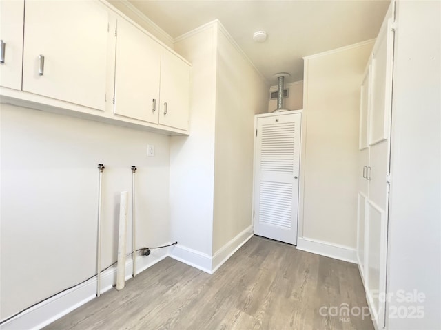 clothes washing area featuring light wood-type flooring, cabinet space, baseboards, and ornamental molding