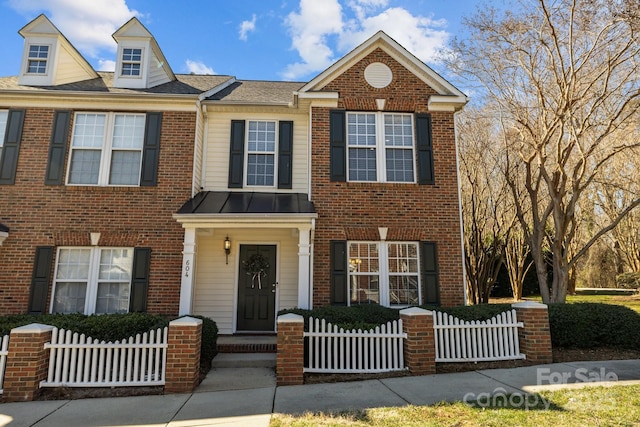 townhome / multi-family property with a fenced front yard, a standing seam roof, and brick siding