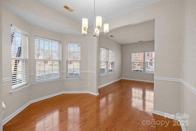 unfurnished dining area featuring an inviting chandelier, baseboards, visible vents, and wood finished floors
