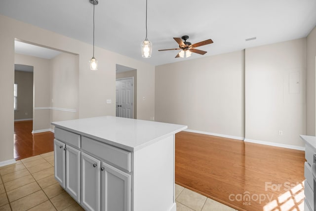 kitchen featuring light tile patterned floors, ceiling fan, light countertops, a center island, and decorative light fixtures