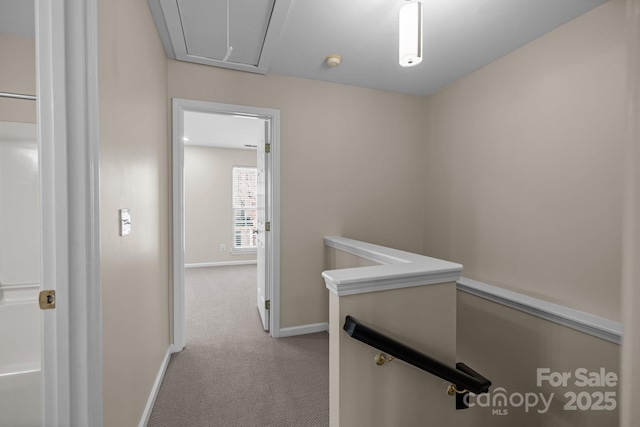 hallway featuring baseboards, carpet, an upstairs landing, and attic access