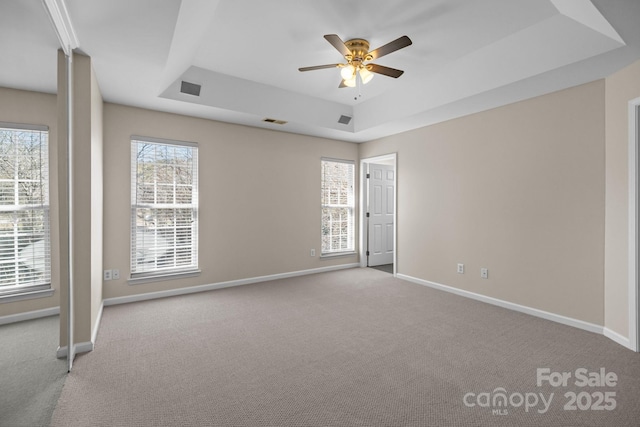 carpeted spare room with baseboards, visible vents, a raised ceiling, and a ceiling fan