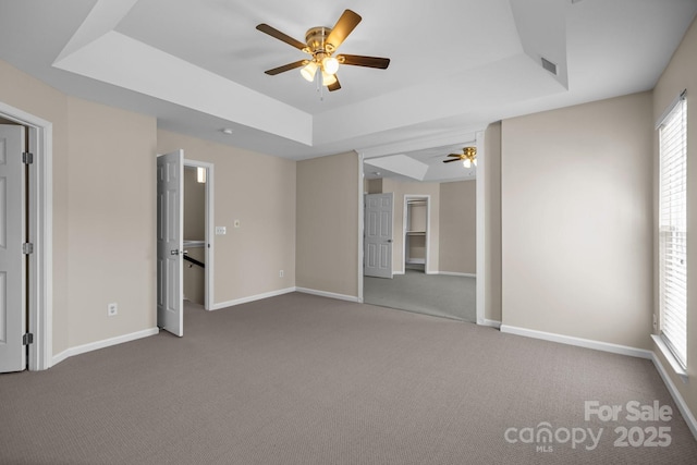 unfurnished bedroom featuring carpet floors, a raised ceiling, visible vents, a ceiling fan, and baseboards