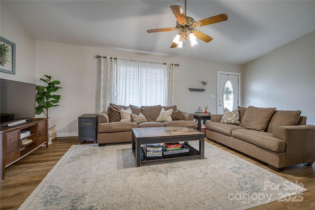 living area with lofted ceiling, ceiling fan, wood finished floors, and baseboards