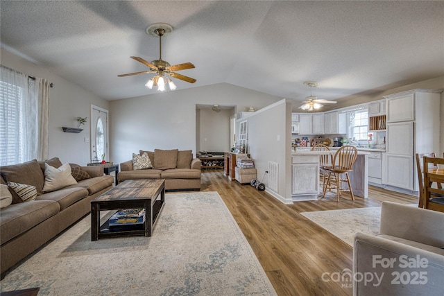 living room featuring visible vents, a ceiling fan, vaulted ceiling, a textured ceiling, and light wood-type flooring