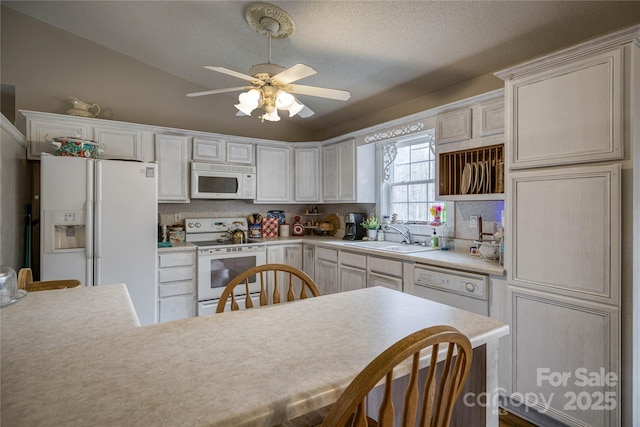 kitchen featuring white appliances, a ceiling fan, vaulted ceiling, light countertops, and a sink