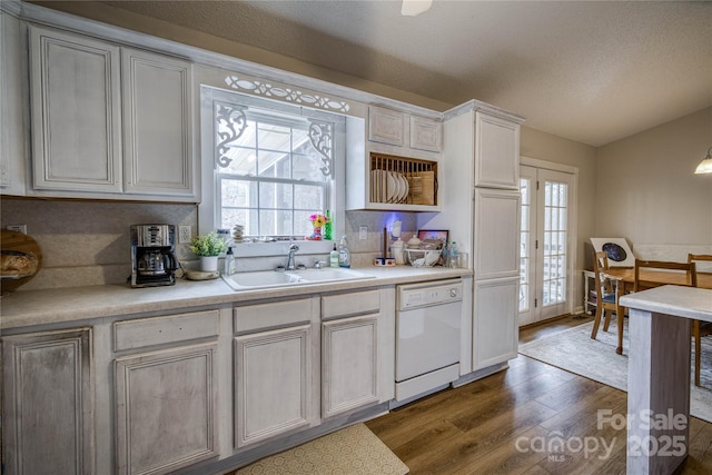 kitchen with a textured ceiling, white dishwasher, a sink, light countertops, and dark wood-style floors