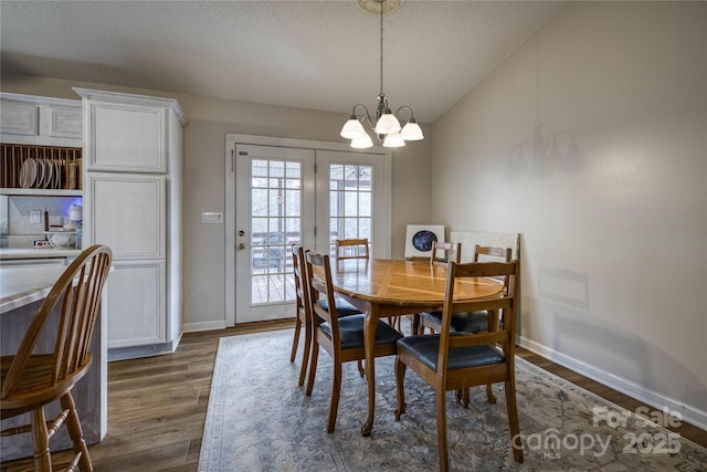 dining area with dark wood-style floors, a notable chandelier, vaulted ceiling, a textured ceiling, and baseboards